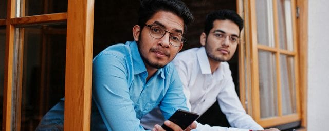 Two south asian men's posed at business meeting in cafe. Indians work together using various gadgets, having conversation. Holding mobile phones.